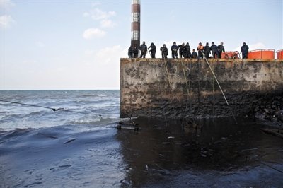 昨日，山東青島，清污人員正在海邊清理油污。