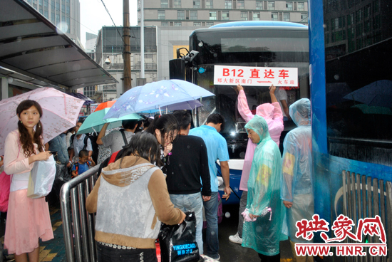 公交志愿者雨中高舉“B12-直達車”指示牌疏導(dǎo)返校學(xué)生乘車