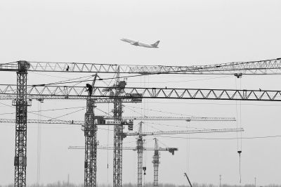 空中是起飛的飛機(jī)，下面是T2航站樓工地上林立的塔吊