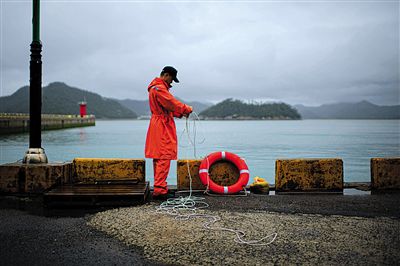 7月6日，韓國(guó)珍島，一名海岸警察在港口系救生圈。4月，客輪在珍島近海發(fā)生沉船事故后，仍有11人下落不明。