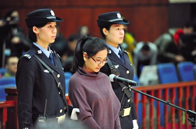被告人盧梅低著頭，站在朝陽法院刑事審判庭的被告席上。